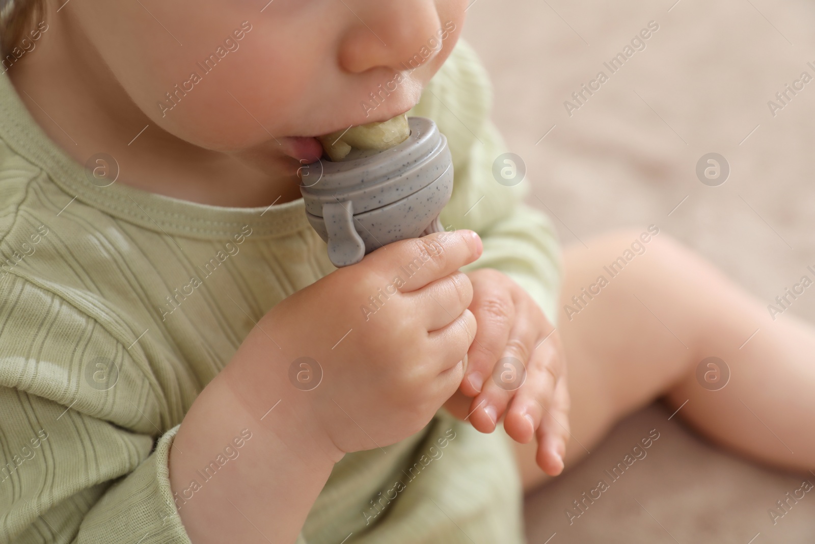 Photo of Baby girl with nibbler on light background, closeup