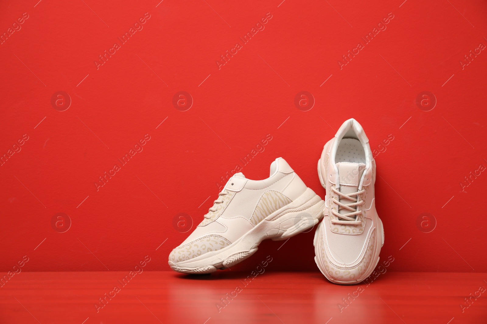 Photo of Stylish women's sneakers on wooden table near red wall, space for text