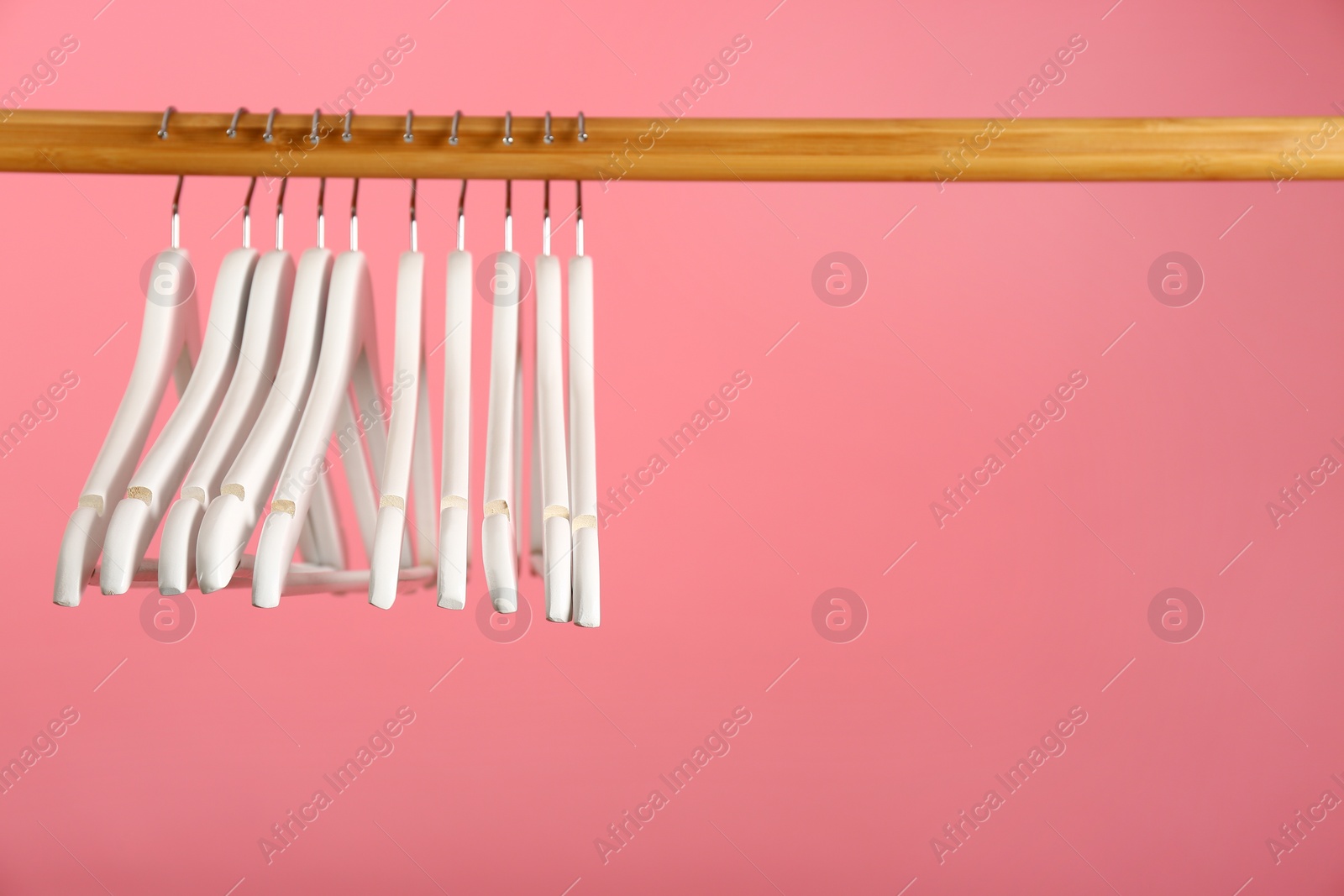 Photo of Empty clothes hangers on wooden rail against color background. Space for text