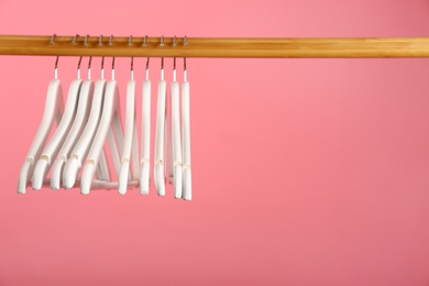 Photo of Empty clothes hangers on wooden rail against color background. Space for text