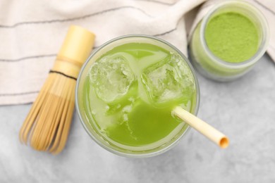 Photo of Glass of delicious iced green matcha tea, powder and bamboo whisk on light grey table, flat lay