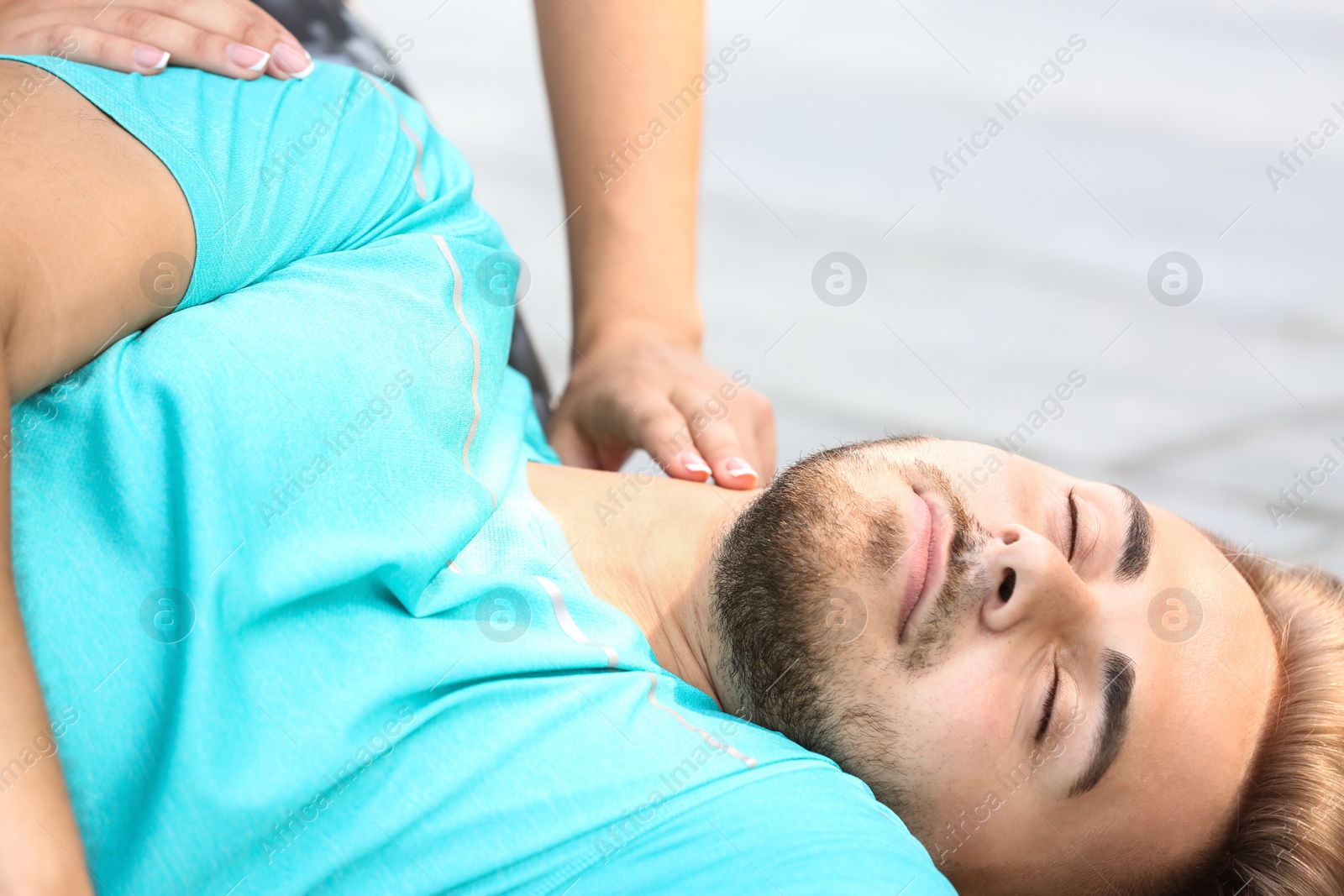 Photo of Woman checking pulse of unconscious man outdoors
