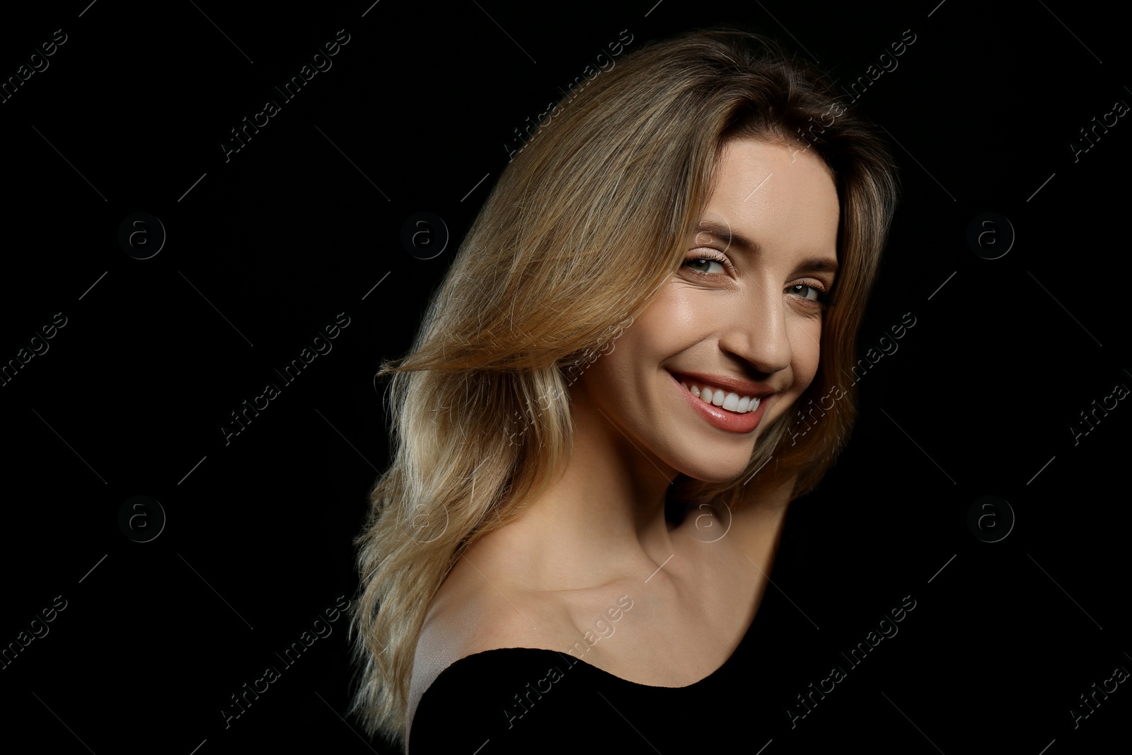 Photo of Portrait of happy young woman with beautiful blonde hair and charming smile on black background