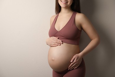 Pregnant young woman touching belly on beige background, closeup
