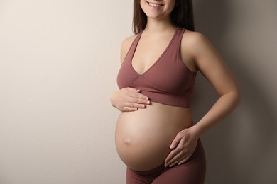 Photo of Pregnant young woman touching belly on beige background, closeup