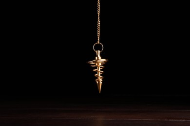 Photo of Stylish pendulum above wooden table on black background. Hypnotherapy session