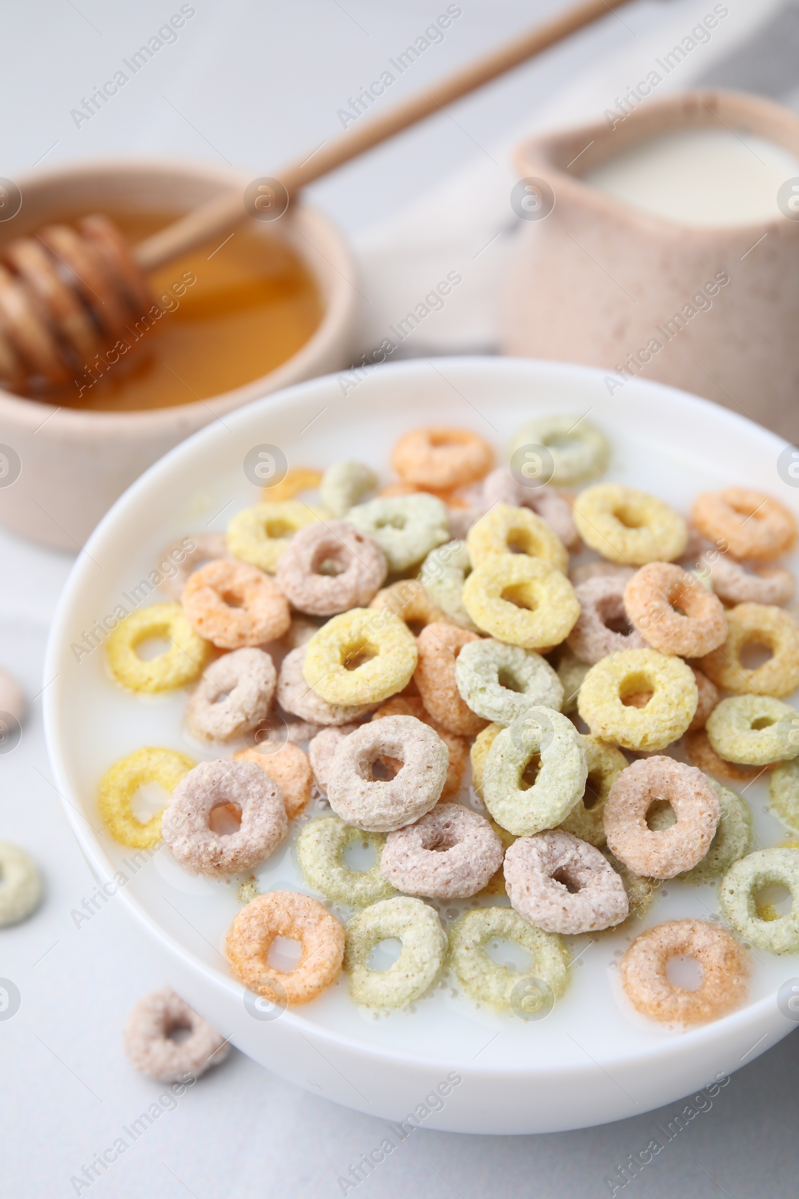 Photo of Cereal rings and milk in bowl on white table, closeup