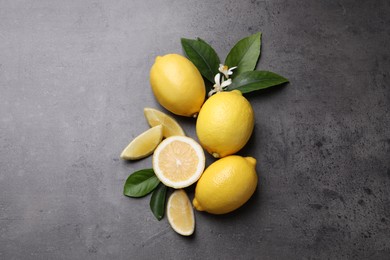 Photo of Many fresh ripe lemons with green leaves and flowers on grey table, top view. Space for text