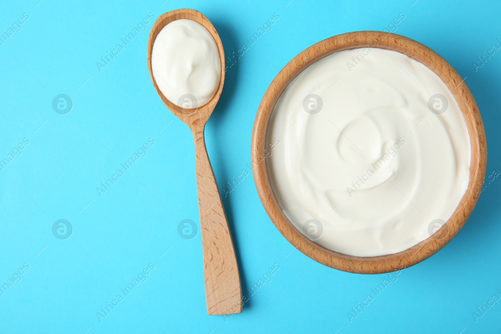 Photo of Wooden bowl and spoon of sour cream on light blue background, flat lay