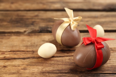 Photo of Sweet chocolate eggs with bows on wooden table. Space for text