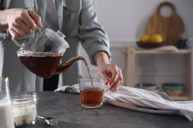 Photo of Woman pouring hot tea into cup at grey table, closeup. Space for text