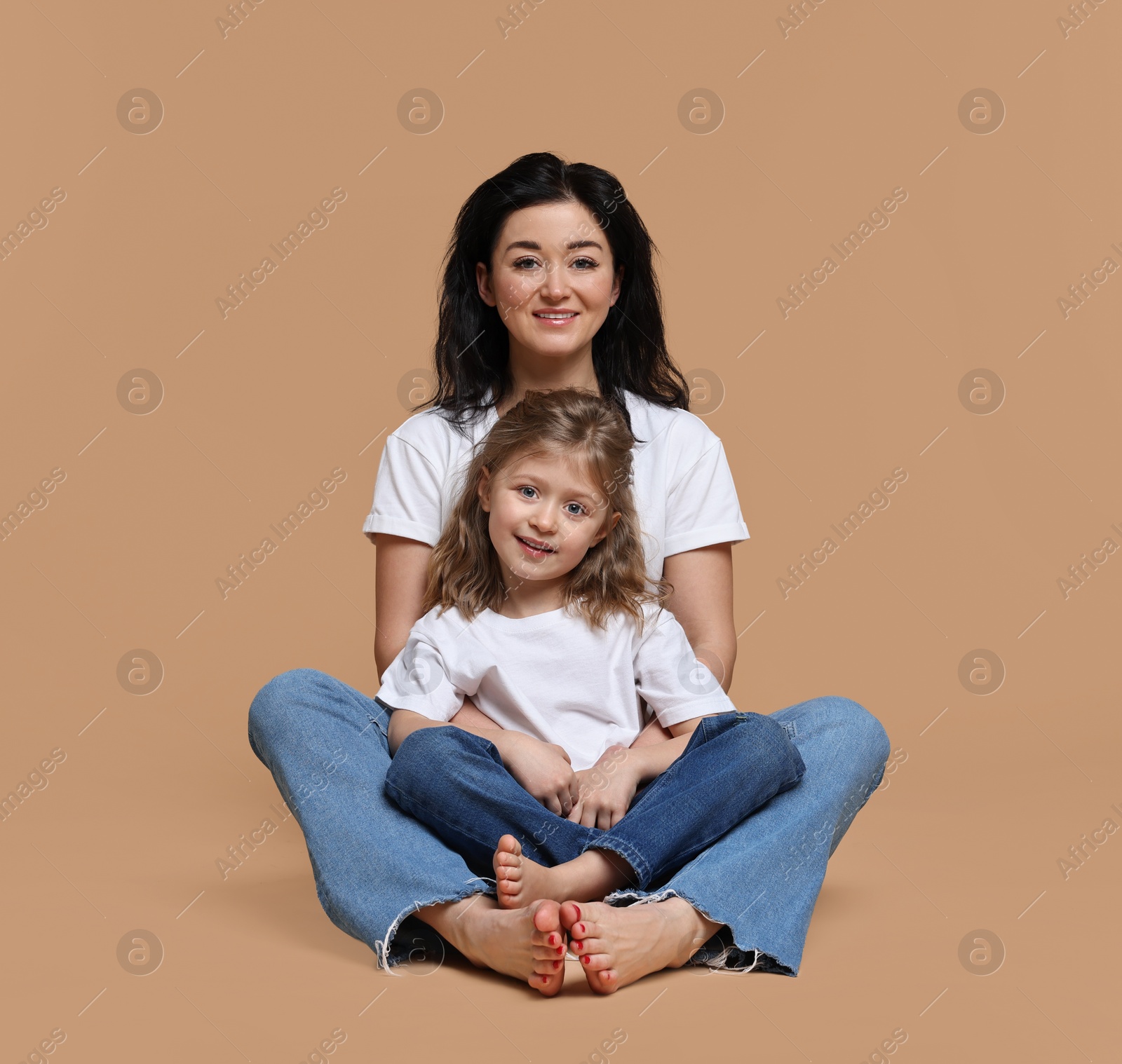 Photo of Beautiful mother with little daughter sitting on beige background