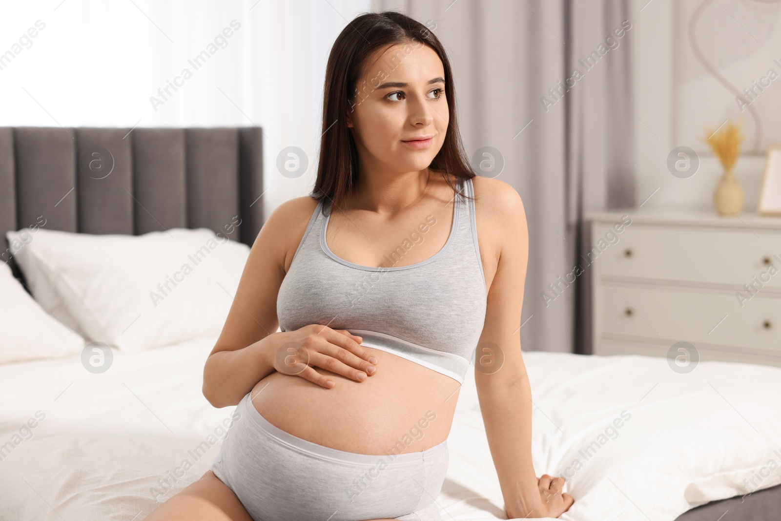 Photo of Beautiful pregnant woman in comfortable maternity underwear on bed at home