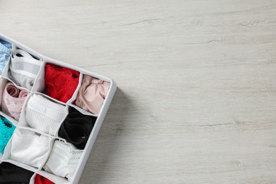 Photo of Organizer with folded women's underwear on light wooden table, top view. Space for text
