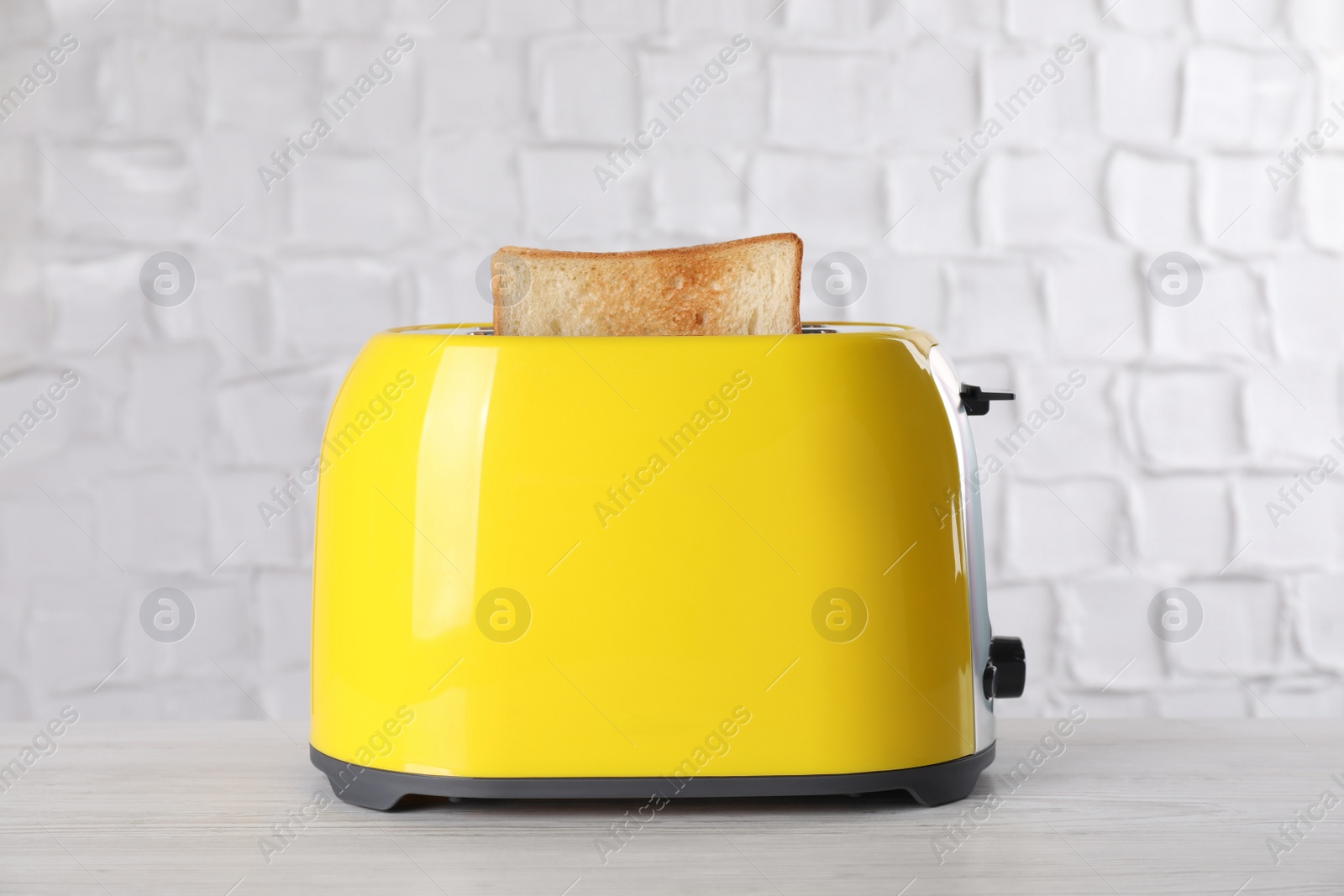 Photo of Modern toaster with slice of bread on white wooden table