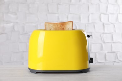 Photo of Modern toaster with slice of bread on white wooden table