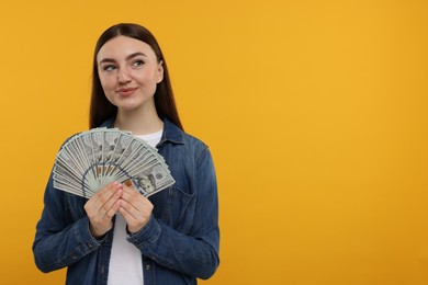 Woman with dollar banknotes on orange background, space for text