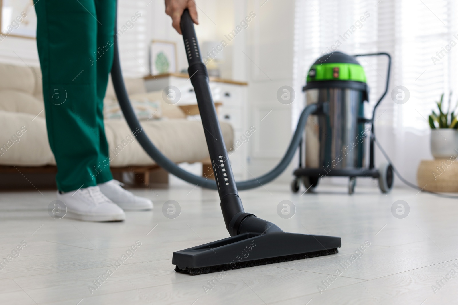 Photo of Professional janitor vacuuming floor in living room, closeup