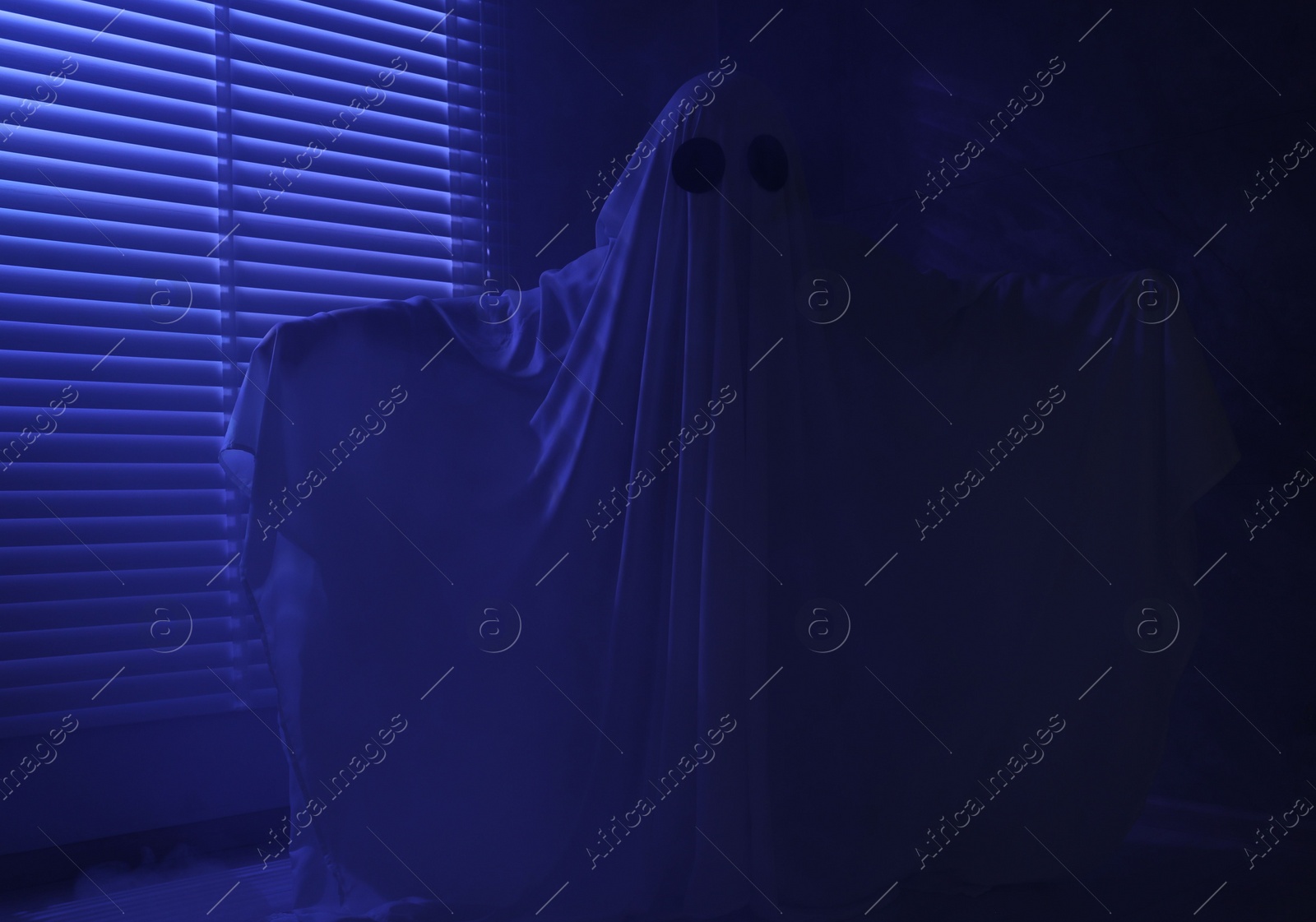 Photo of Creepy ghost. Woman covered with sheet near window in blue light