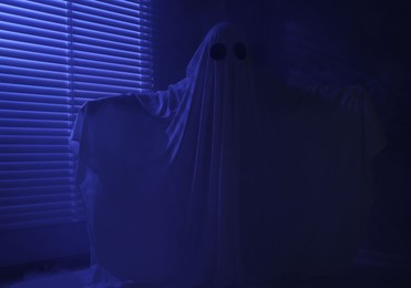 Photo of Creepy ghost. Woman covered with sheet near window in blue light