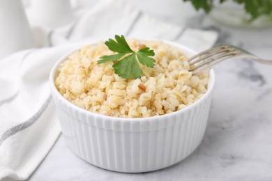 Photo of Cooked bulgur with parsley in bowl on white marble table, closeup