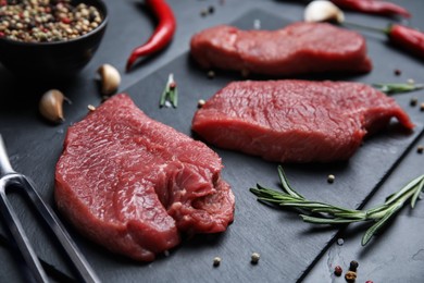 Photo of Fresh raw meat steaks and spices on black table, closeup