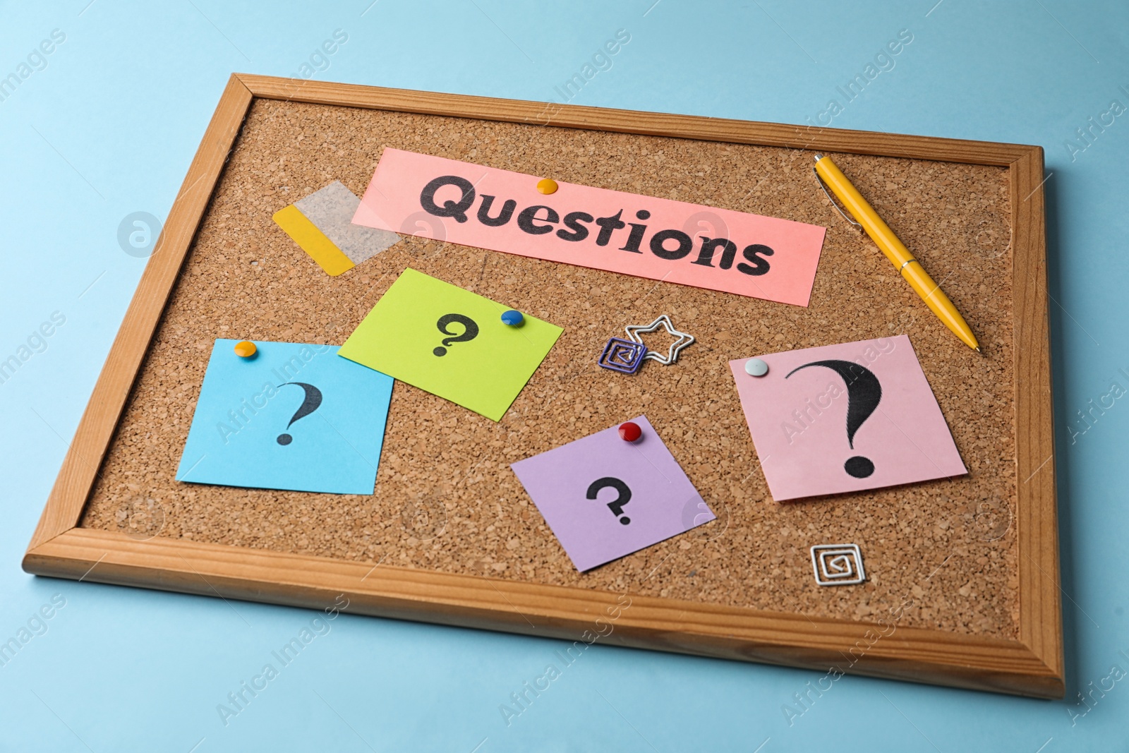 Photo of Cork board with word QUESTIONS and query marks on light blue background