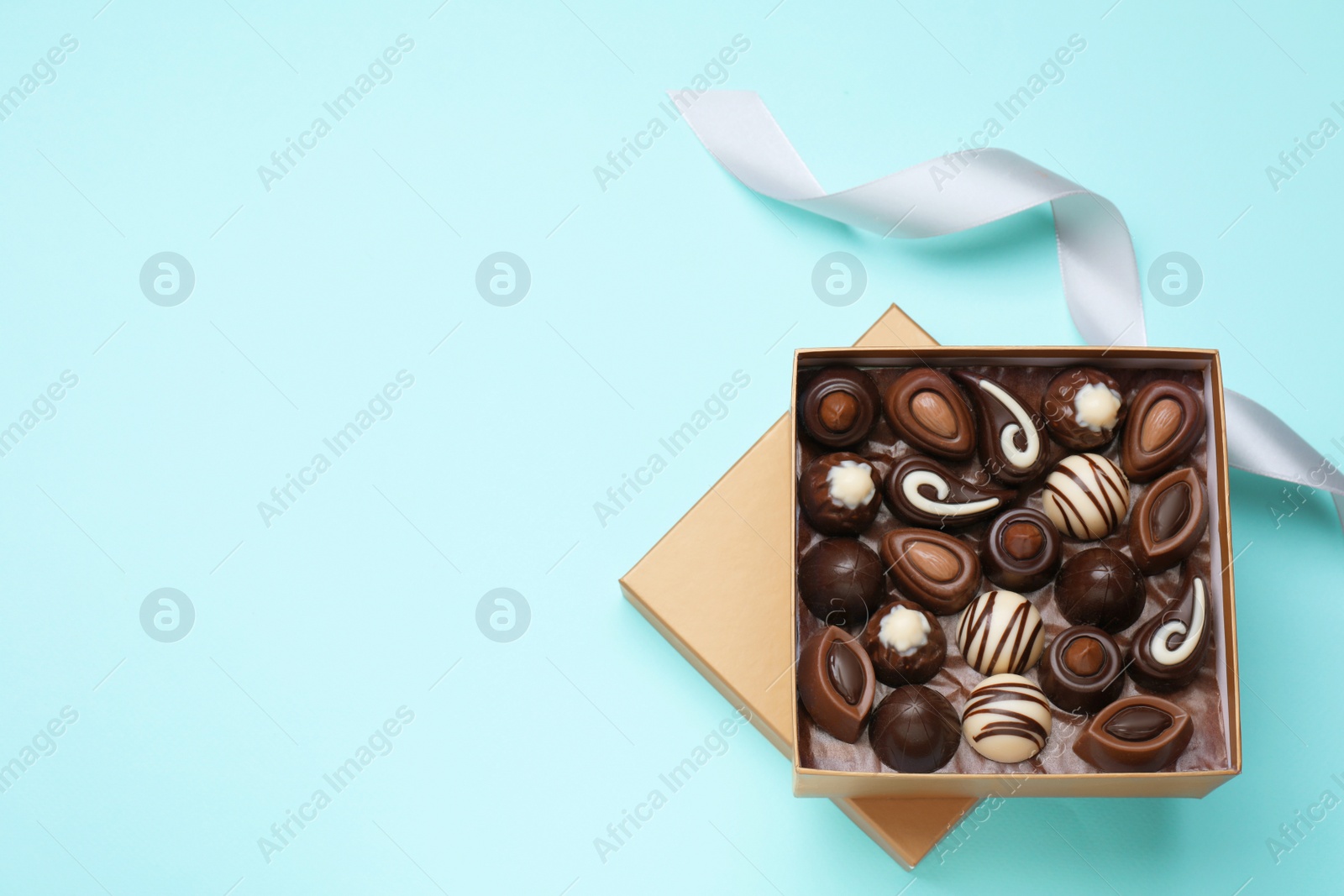 Photo of Open box of delicious chocolate candies on light blue background, flat lay. Space for text