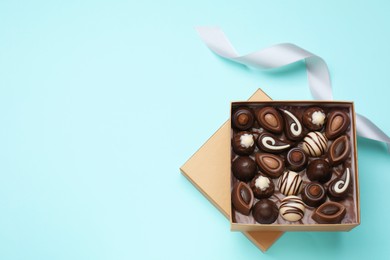 Photo of Open box of delicious chocolate candies on light blue background, flat lay. Space for text