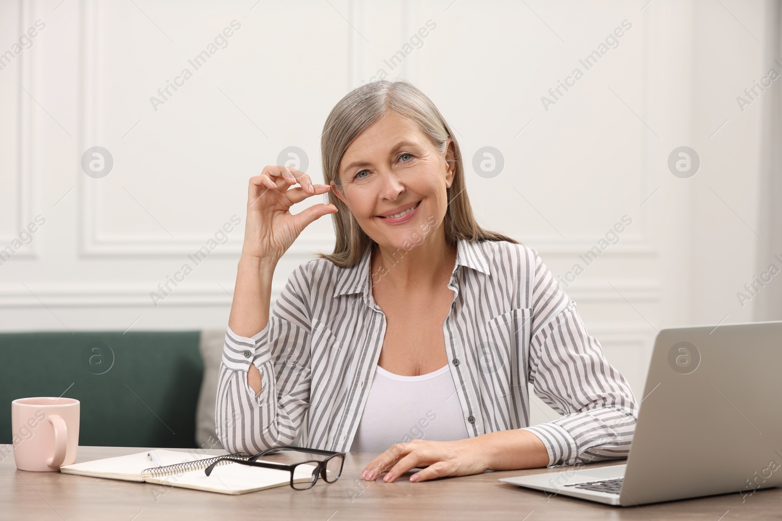 Photo of Menopause, hormone replacement therapy. Happy woman holding pill at wooden table indoors