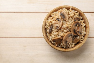 Delicious pearl barley with mushrooms in bowl on. wooden table, top view. Space for text