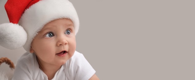 Image of Cute baby wearing Santa hat on light grey background, banner design with space for text. Christmas celebration