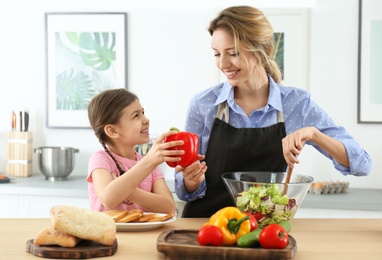 Young nanny with cute little girl cooking together in kitchen