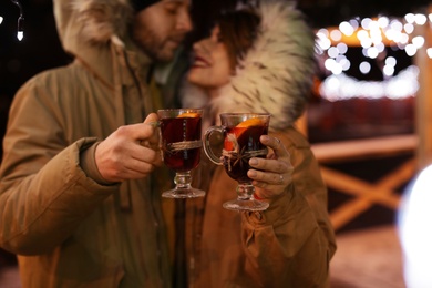 Photo of Young couple with cups of mulled wine at winter fair