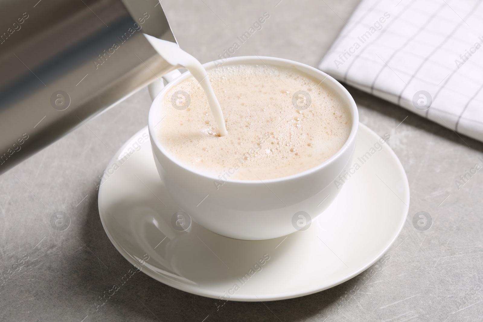 Photo of Pouring milk into cup of coffee on grey table