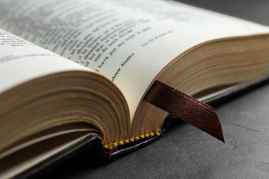 Photo of Open hardcover Bible on black table, closeup. Religious book