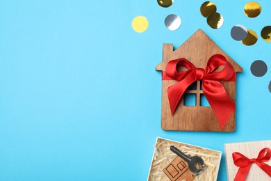 Photo of Wooden house model and key in gift box on light blue background, flat lay with space for text. Housewarming party