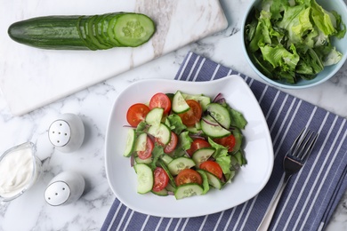 Plate of vegetarian salad with cucumber, tomato, lettuce and onion served on table, flat lay