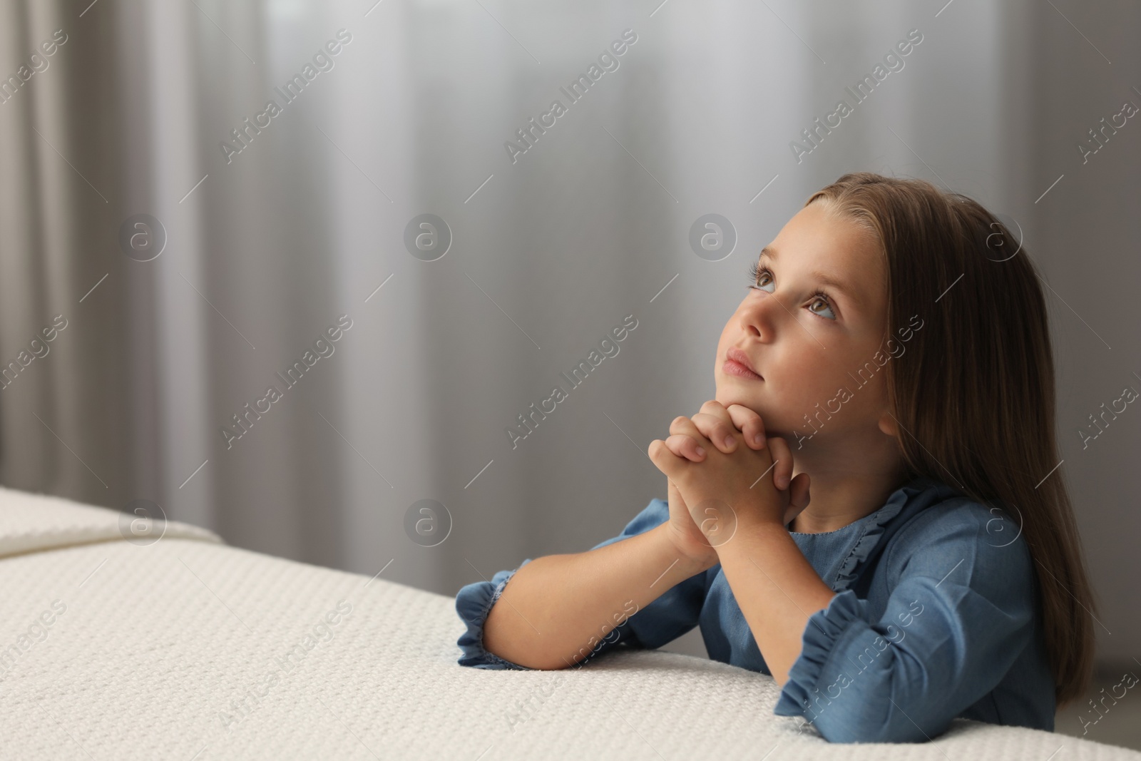 Photo of Cute little girl with hands clasped together saying bedtime prayer in bedroom. Space for text