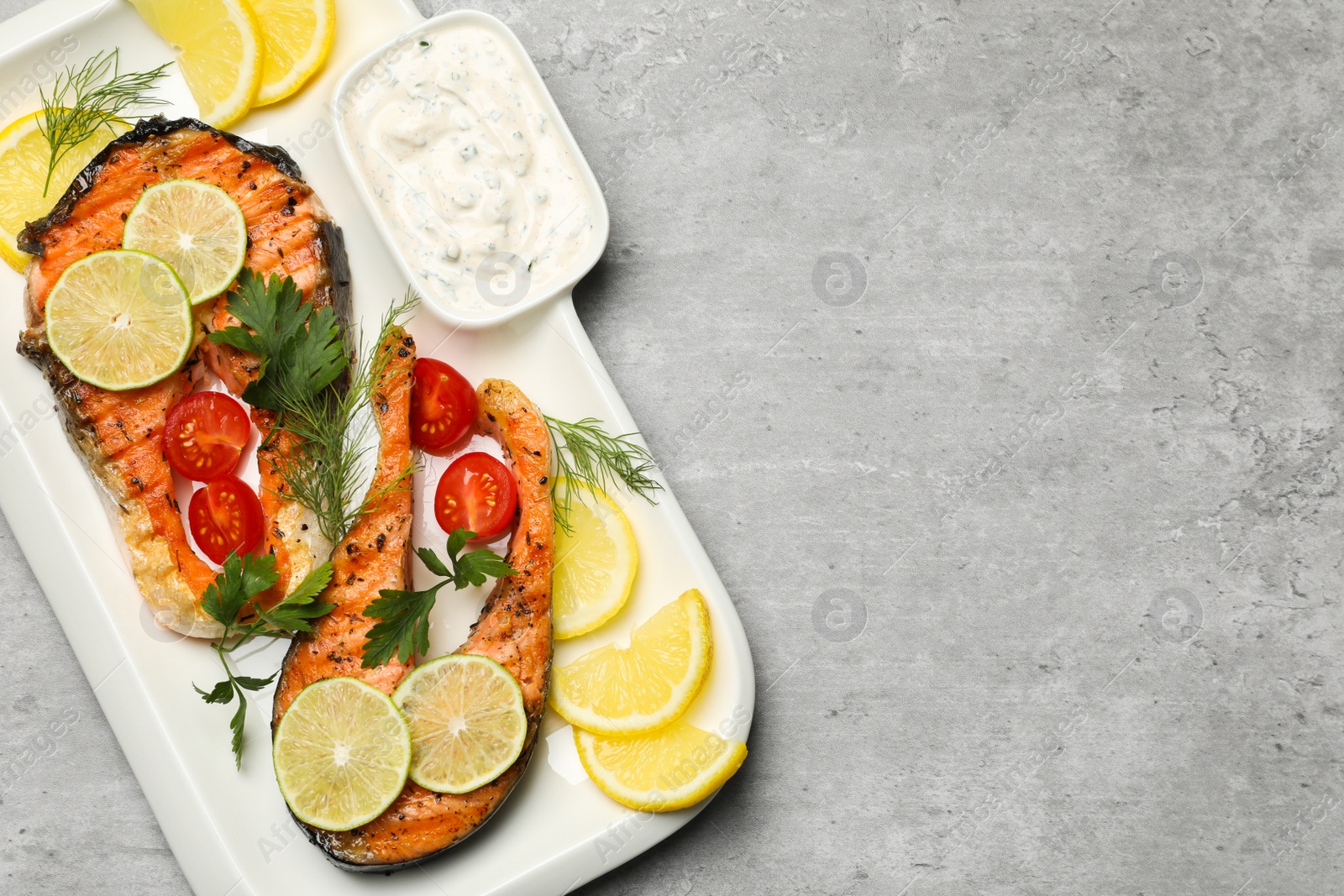 Photo of Tasty grilled salmon steaks and ingredients on light grey table, flat lay. Space for text