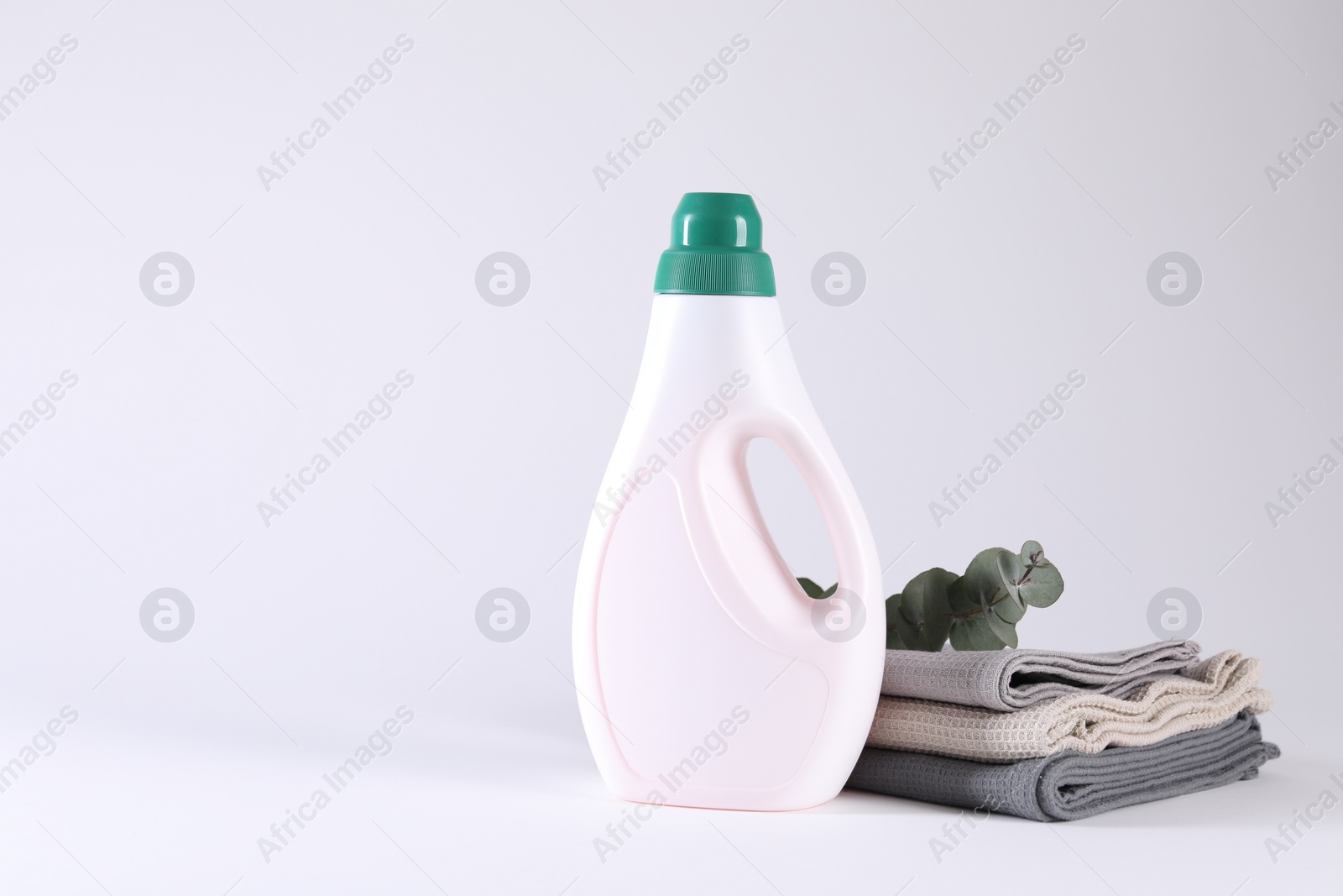 Photo of Bottle of cleaning product, rags and floral decor on light background