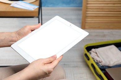 Woman using modern tablet while packing suitcase for summer vacation at home, closeup