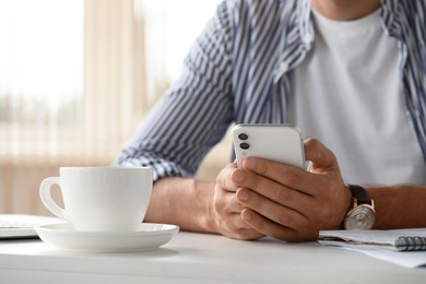 Photo of Man sitting at table and using smartphone in room, closeup