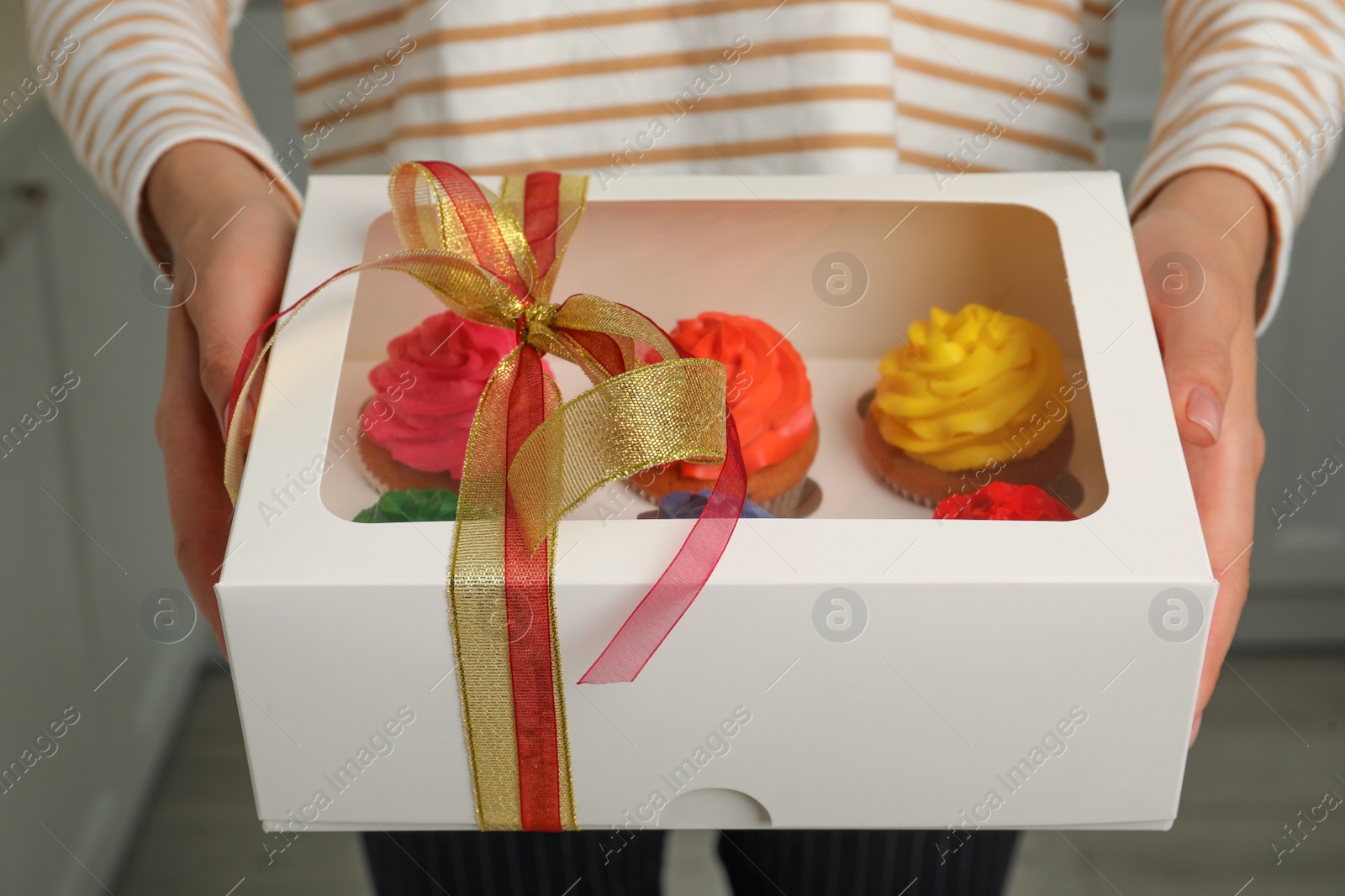 Photo of Woman holding box with delicious colorful cupcakes indoors, closeup