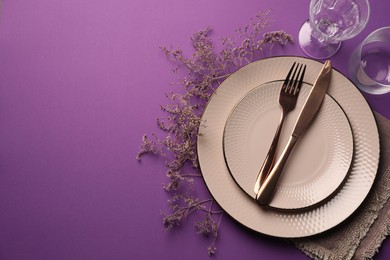 Stylish table setting. Plates, cutlery, glasses and floral decor on purple background, flat lay with space for text