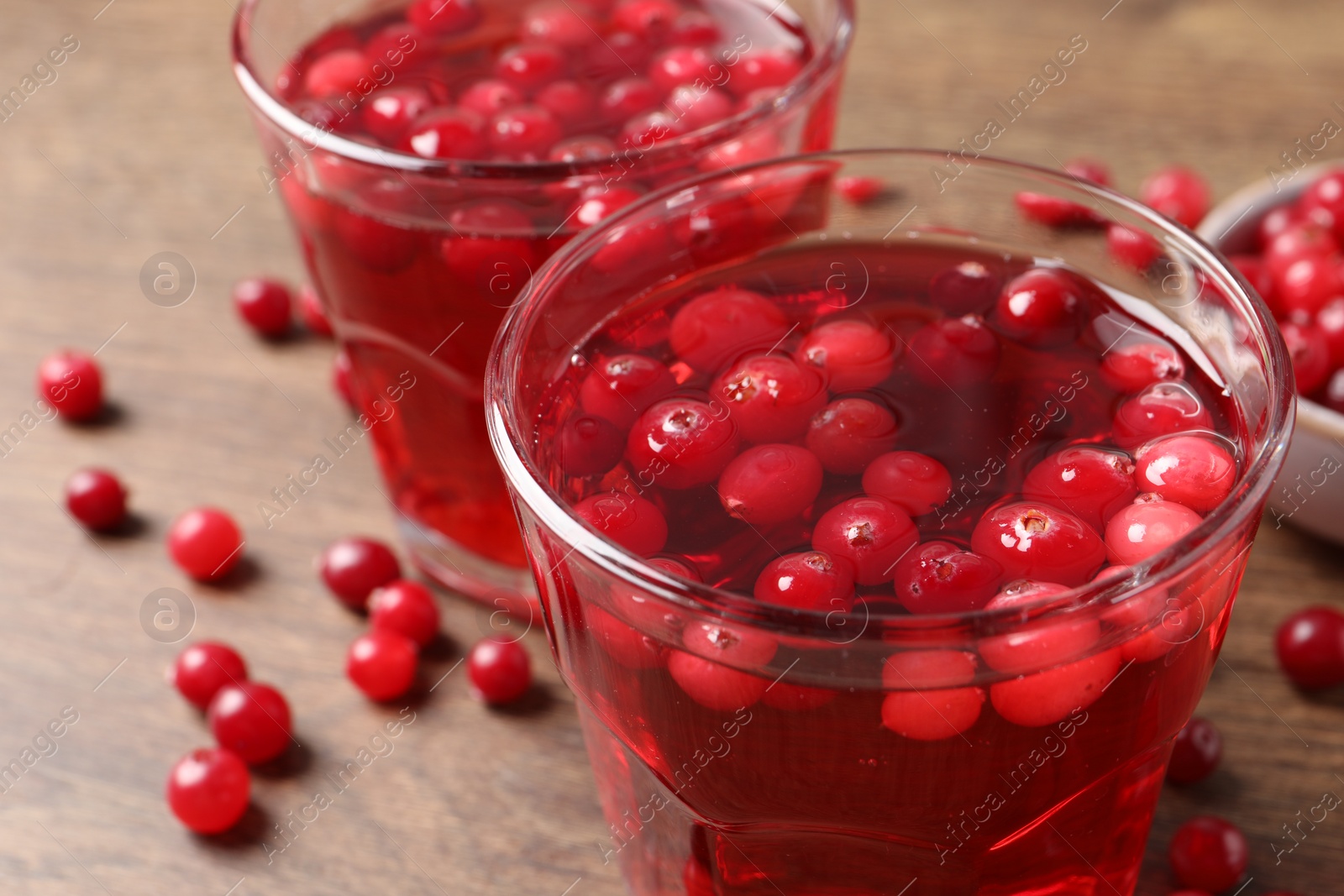 Photo of Tasty cranberry juice in glasses and fresh berries on wooden table, closeup