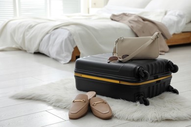 Suitcase packed for trip, shoes and fashionable accessories on floor in bedroom