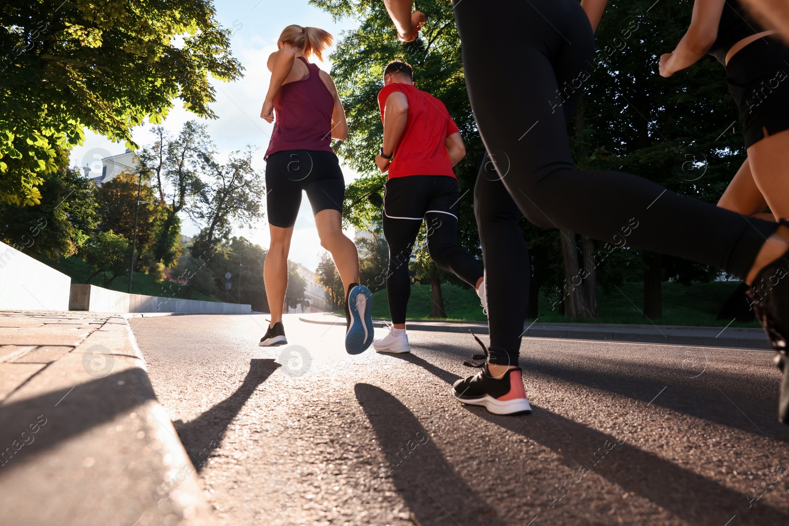 Photo of Group of people running outdoors on sunny day, back view