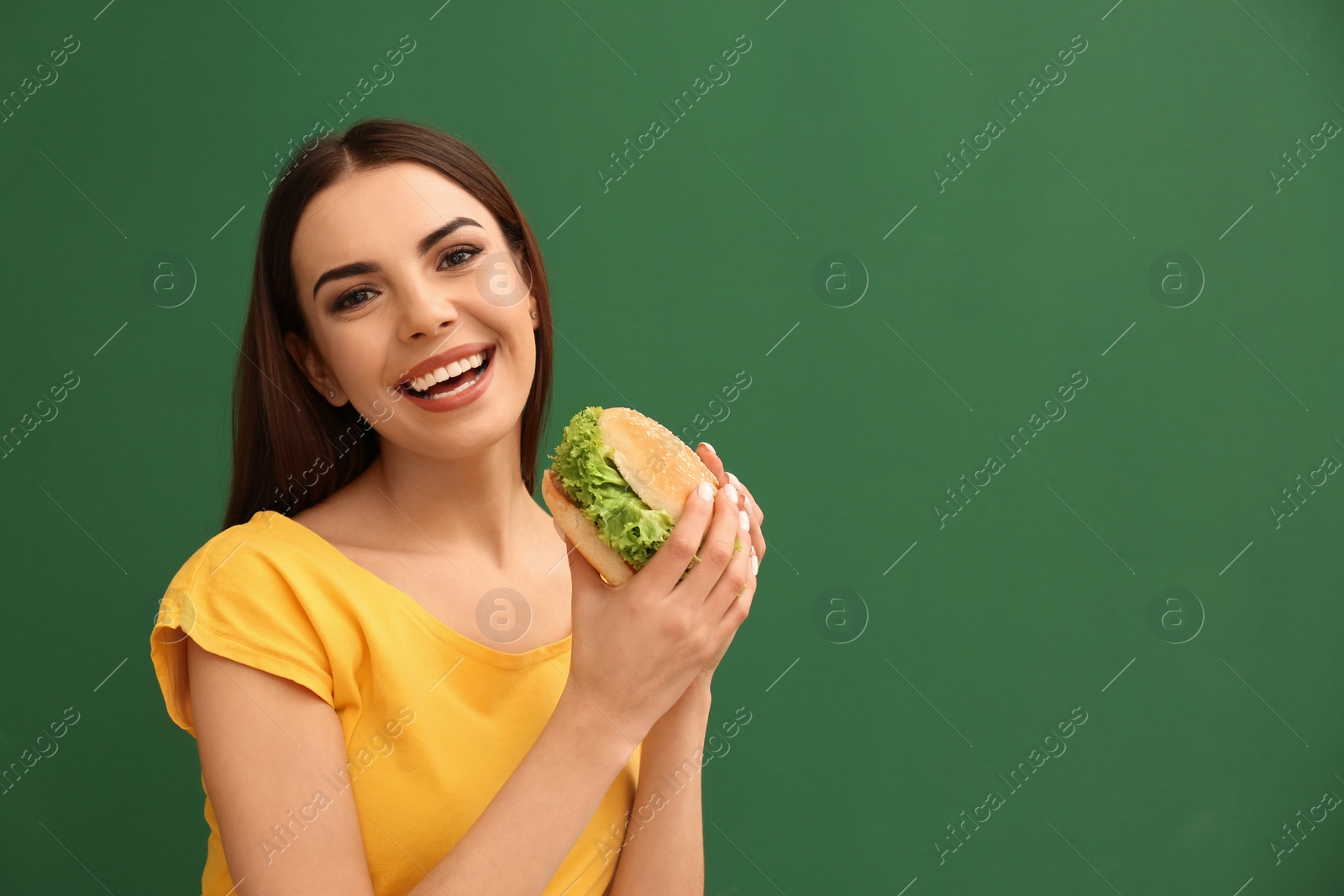 Photo of Young woman eating tasty burger on color background. Space for text