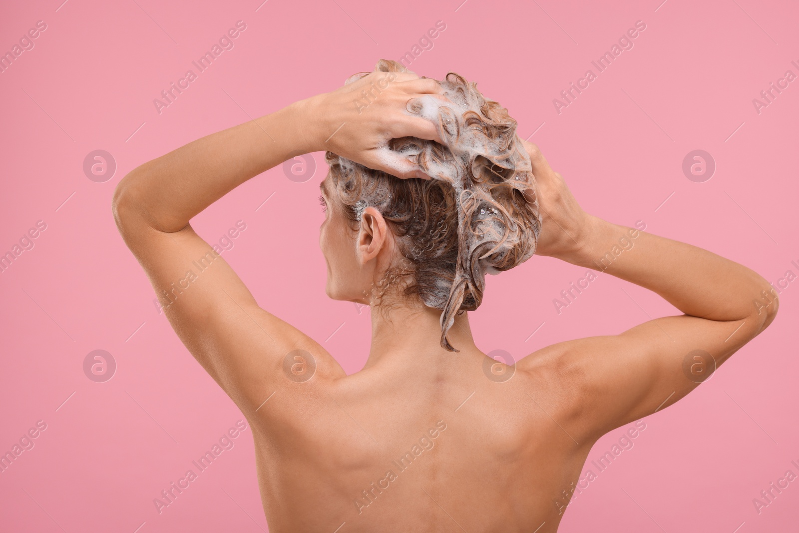 Photo of Woman washing hair on pink background, back view